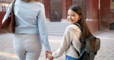 Güzel, beyaz bir kadın, okulun yanında güzel, mutlu bir kızla yürüyor. Sırt çantalı, annesiyle yürüyen ve kameraya dönen neşeli genç kız öğrencinin portresi. Aile kavramı