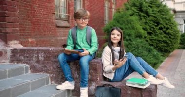 Tabletli şirin beyaz çocuk ve açık havada okulun yanında otururken kameraya gülümseyen akıllı telefonlu kız öğrenci. Okul bahçesinde ellerinde aletlerle neşeli öğrencilerin keyfi yerindeydi..
