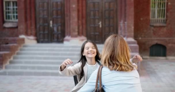 Portret szczęśliwej nastolatki uśmiechającej się i biegającej do matki po zajęciach w pobliżu szkoły. Tył białej kobiety spotyka córkę ze szkoły na świeżym powietrzu i przytula się w dobrym nastroju. Koncepcja rodziny — Wideo stockowe