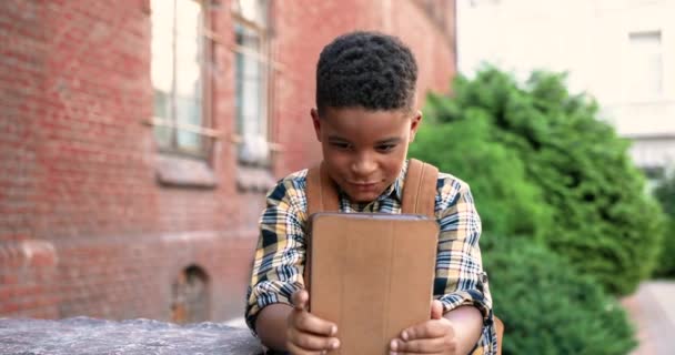 Portret skoncentrowanego afroamerykańskiego nastolatka stukającego i przeglądającego tablety na świeżym powietrzu. Słodki mężczyzna junior student za pomocą urządzenia w pobliżu szkoły i patrząc na ekranie. Uczeń za pomocą gadżet Uczeń koncepcja — Wideo stockowe