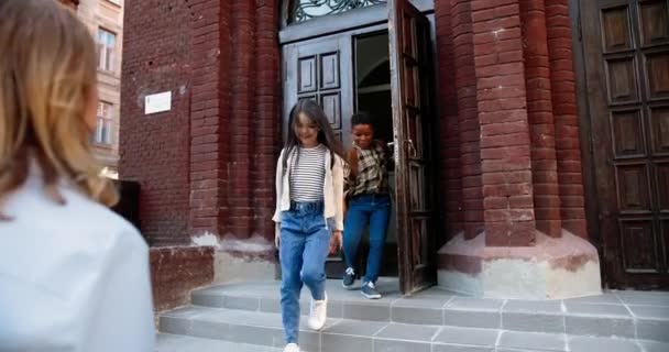 Multi-ethnic happy junior students leaving school. Parents meet children from school. Caucasian beautiful woman hugs schoolgirl. African American handsome man hugging boy after classes. Love concept — Stock Video