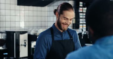 Kafkasyalı neşeli genç barmen gülümsüyor, kafede cam silerken Afrikalı Amerikalı bir müşteriyle konuşuyor. Karışık ırk erkekleri güzel sohbetler yapıyor. Arka taraf. çok ırklı müşteri ve barmen