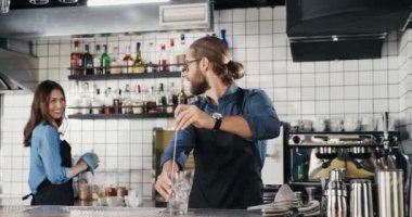 Beyaz, yakışıklı ve neşeli bir barmen. Buzlu içki hazırlıyor ve bayan meslektaşlarına gülümsüyor. Garson ve garson konuşuyor. Barmen, barda buzla kokteyl yapıyor..