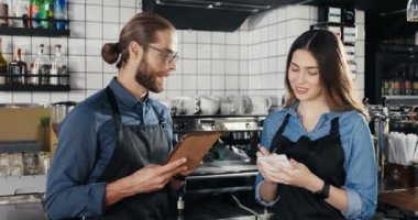 Tablet tableti taşıyan beyaz tenli yakışıklı barmen ve sipariş ya da alışveriş listesi yazan kadın barmen. Bar mutfağında. Garson ve garson kafe için menü hazırlıyorlar..