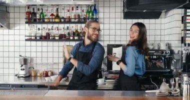 Kafkasyalı, genç, neşeli, önlüklü iki barmen kafede neşe içinde dans ediyor. Yakışıklı garson ve güzel garson iş yerinde mutlu mesut eğleniyor. Erkek ve kadın iş arkadaşları