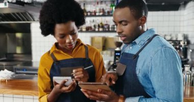 Önlüklü, Afro-Amerikalı, yakışıklı, genç barmen, elinde tablet var ve kadın barolar sipariş listesi ya da bar mutfağından alışveriş yapıyorlar. Garson ve garson kafe için menü hazırlıyorlar.