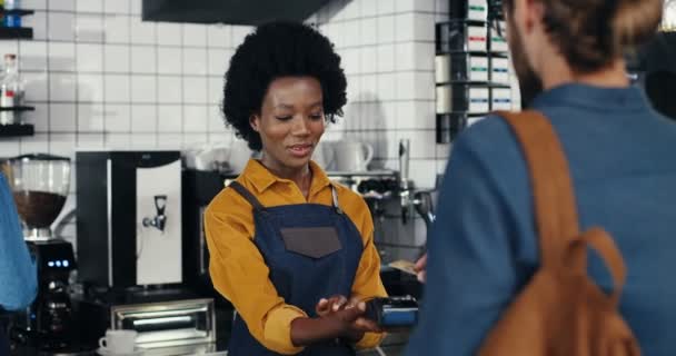 Zadní bělošský klient v kavárně platí kreditní kartou. Míchané rasy. Africká americká barmanka bere objednávky a peníze. Multietnický zákazník a barista. Zaplatit za pití s výplatní páskou. — Stock video