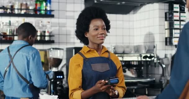 Multiethnic bartender woman and client man. Caucasian male paying with paypass, credit card. Mixed-races. Passing payment at counter. Pay for drink or food in cafe. African American waitress. — Stock Video