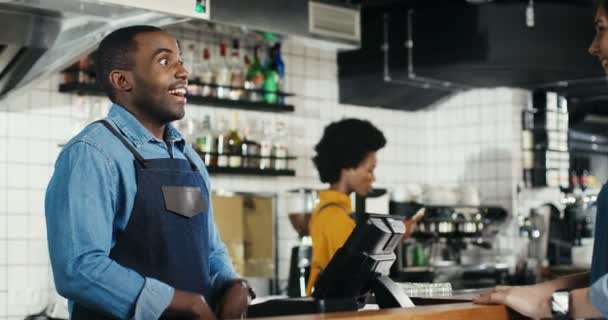 Garçom afro-americano alegre servindo café e conversando com mulher caucasiana no balcão no café. Homem barrista ter boa conversa com o cliente. Homem barman conversando com cliente feminino Multiétnico — Vídeo de Stock