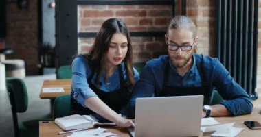 Masada oturan beyaz bir çift ve masa başı iş hesaplamaları. Erkek ve kadın, kafenin masraflarını ve zararlarını hesaplıyor. Dizüstü bilgisayardaki kilitleme işleminden sonra tekrar aç. Küçük girişimcilik.