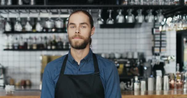 Retrato de homem bonito jovem caucasiano barista em pé no balcão no bar, olhando para a câmera e cruzando as mãos. Garçom sorrindo no café com equipamentos de bebidas em segundo plano. Aumento de zoom. — Vídeo de Stock