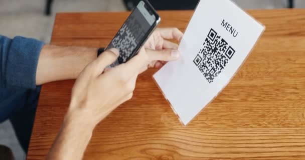 Close-up van zwarte smartphone in blanke mannelijke handen, terwijl de klant in cafe scannen QR-code aan tafel en leesmenu. Man klant met behulp van telefoon en technologieën om orde te maken in de bar. Pandemisch concept. — Stockvideo