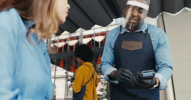 Cliente femenino caucásico en cafetería terraza al aire libre y abogado afroamericano masculino en máscaras hablando. Cliente mujer en restaurante pagando con tarjeta de crédito al aire libre. Razas mixtas. Multiétnico. Pandemia. — Vídeo de stock