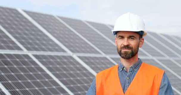 Retrato del alegre ingeniero caucásico en la granja de baterías solares. Hombre barbudo guapo de uniforme mirando brazos cruzados sobre su pecho y sonriendo. — Vídeo de stock