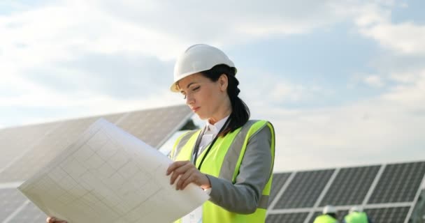 Retrato de hermosa mujer tecnóloga en uniforme con casco protector. Mujer de negocios mirando plan de papel colocación de paneles solares. — Vídeos de Stock