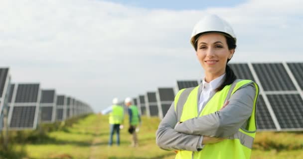 Portrét krásné ženské techničky stojící mezi solárními panely s rukama zkříženýma na prsou. Žena v ochranné přilbě a uniformě s úsměvem na kameru. — Stock video