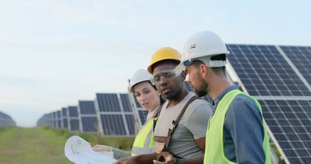 Tři zaměstnanci alternativní elektrárny chodí a mluví o schématu solárních panelů. Týmová práce. Skupina specialistů. Kamera sleduje lidi. — Stock video