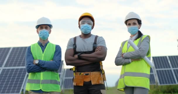 Портрет трьох робітників, що стоять на сонячній електростанції в спеціальній уніформі та захисних масках. Концепція безпечного спілкування під час пандемії . — стокове відео