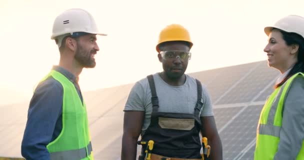 Drie gelukkige medewerkers van de zonnecentrale steken tegelijkertijd hun handen op en schreeuwen van vreugde. Mensen zijn tevreden met het resultaat van het verrichte werk. — Stockvideo