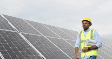 Mutlu güneş enerjisi santrali işçisinin portresi. İnşaat şemaları ve planlarıyla rulo kağıt taşıyor..