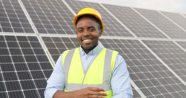 Retrato de un joven guapo artesano afroamericano con casco protector. Hombre feliz posando ante la cámara sonriendo. Movimiento lento. — Vídeos de Stock