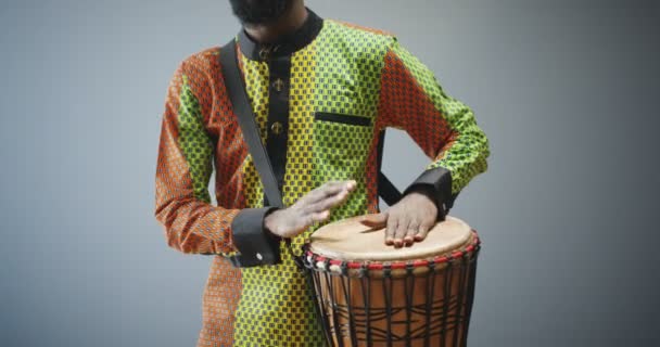 Portrait de musicien afro-américain mâle tapotant sur le tambour et souriant joyeusement à la caméra. Bel homme en tenue traditionnelle jouant sur le bongo avec un visage heureux. Musicien avec instrument de musique. — Video