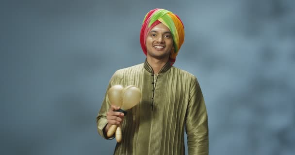 Portret van de jonge Hindoe mannelijke muzikant in tulband glimlachend en spelend op jachthavens. Gelukkige man uit India die muziekinstrumenten vasthoudt en ritme maakt op muziek terwijl hij ze schudt. Feestelijk concept. — Stockvideo