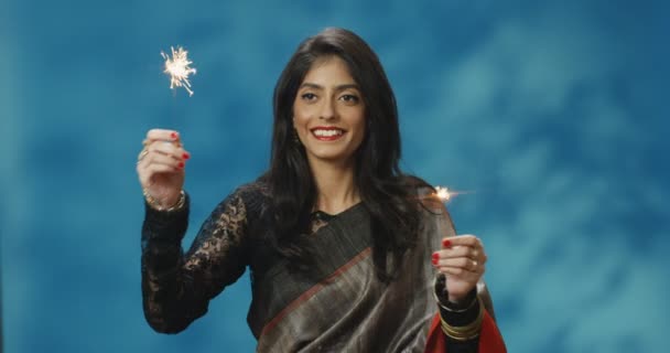 Happy beautiful Hindu young woman in traditional outfit smiling to camera and holding Bengal lights on New Year Eve celebration. Portrait of girl waving with sparklers. Cultural traditions concept. — Stock Video