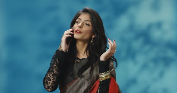 Молода красива індуська жінка в традиційному одязі весело розмовляє по мобільному телефону і посміхається. Приваблива жінка з Індії розмовляє по мобільному телефону. Дівчинка розмовляє по телефону з посмішкою.. — стокове відео