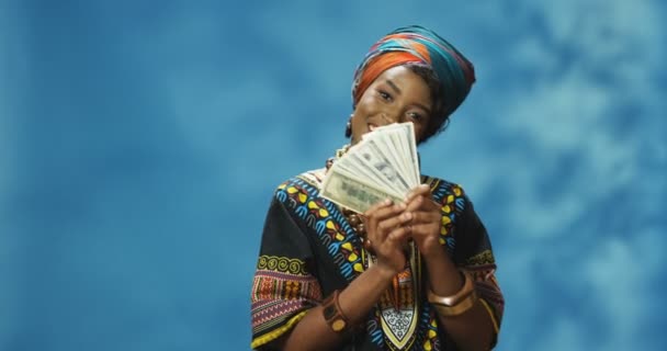 Retrato de una joven afroamericana hermosa vestida con ropa tradicional contando dinero delante de la cámara. Atractiva mujer sosteniendo billetes en dólares y mostrándolos. concepto de niña rica. — Vídeos de Stock