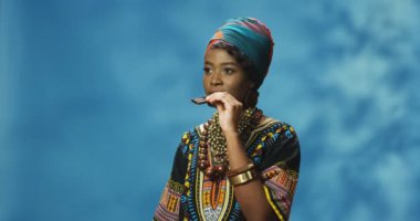 Geleneksel giysiler içinde, siyah çikolata yiyip gülümseyen güzel Afro-Amerikan bir kadın. Güzel, şık bir kız tatlı yiyor ve zevk alıyor..