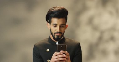 Sakallı, siyah ceketli yakışıklı Hindu genç adam akıllı telefondan mesaj atıyor ve sohbet ediyor. Çekici bir erkek cep telefonuyla dinleyip daktilo kullanıyor. Cep telefonu ve kaydırma kullanan adam.