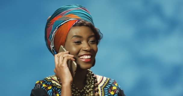 Blisko Afroamerykanów młoda, piękna, wesoła kobieta w tradycyjnych ubraniach rozmawiająca radośnie przez telefon komórkowy i uśmiechnięta. Ładna dziewczyna śmieje się przez komórkę. Rozmowa telefoniczna. — Wideo stockowe