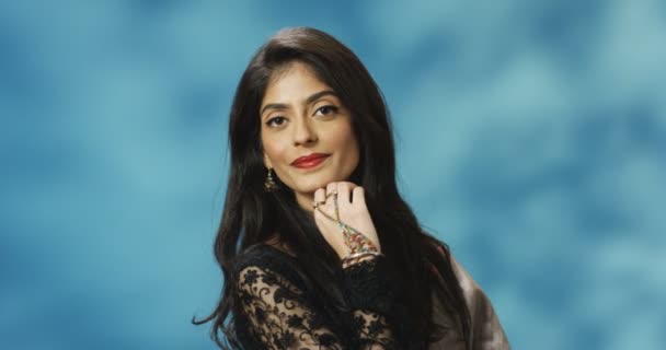 Portrait prise de vue de jeune femme joyeuse et attrayante hindoue en tenue traditionnelle souriant à la caméra sur fond de mur bleu. Jolie femelle élégante avec le sourire dans le style indien. — Video