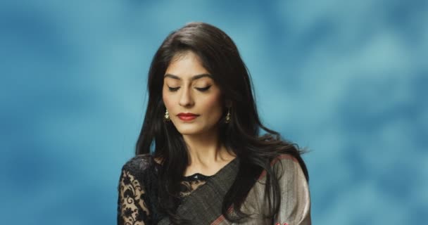Retrato tiro de jovem hindu atraente mulher séria ofendida e egoísta em roupas tradicionais sorrindo para a câmera no fundo da parede azul. Mulher vaidosa muito elegante em estilo indiano. — Vídeo de Stock