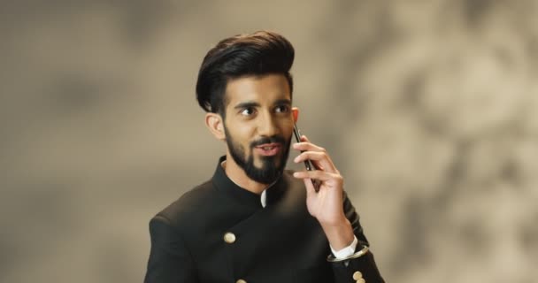 Joven hombre hindú guapo con barba hablando alegremente en el teléfono móvil y sonriendo. Atractivo macho indio feliz hablando por celular. Chico hablar por teléfono con sonrisa. — Vídeos de Stock