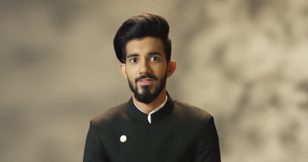 Retrato tiro de jovem alegre e bonito homem hindu com barba e casaco preto olhando para a câmera e sorrindo alegremente. Close up de indiana atraente alegre masculino com sorriso. — Vídeo de Stock