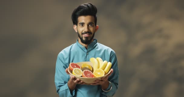 若い陽気な笑顔のハンサムなヒンドゥー教の男が熱帯の果物とプレートを保持し、カメラを見ての肖像写真。魅力的な男ともに果物笑顔幸せ. — ストック動画
