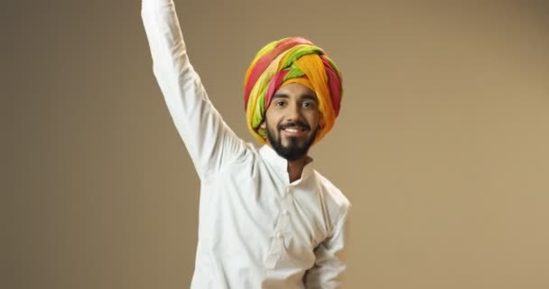 年轻的印度帅哥穿着传统的五颜六色的头巾，带着微笑跳舞和打转。印度男性快乐的舞蹈演员转来转去，玩得很开心. — 图库视频影像