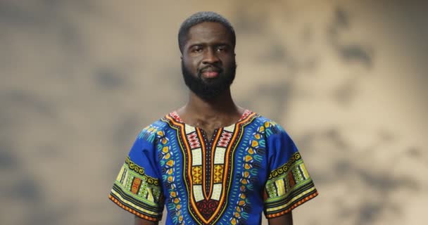 Portretfoto van vrolijke Afro-Amerikaanse jonge knappe man met baard in blauw traditioneel shirt glimlachend naar de camera. Positief stemmingsconcept. Blij tevreden man met glimlach. — Stockvideo