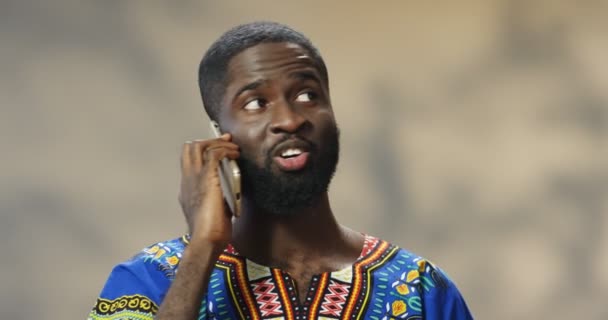 Tæt på smuk munter ung afrikansk amerikansk mand i traditionelt tøj, der taler på mobiltelefon og smiler. Glad mand taler på mobiltelefon. Telefonsamtale. – Stock-video