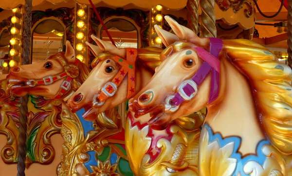 Close up of three antique hand painted carousel horses or gallopers on a fairground ride in a public amusement park. Illuminated background with mirrors. England.