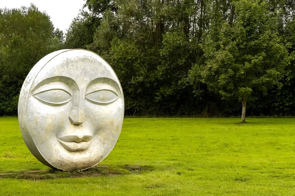 Frilford, Oxfordshire 'da. İngiltere - 30 Haziran 2020: Halka açık bir alanda gözü, burnu ve ağzı olan eskimiş beton yüzlü heykel. Kopyalamak için alanı olan soyut resmi düzenle.