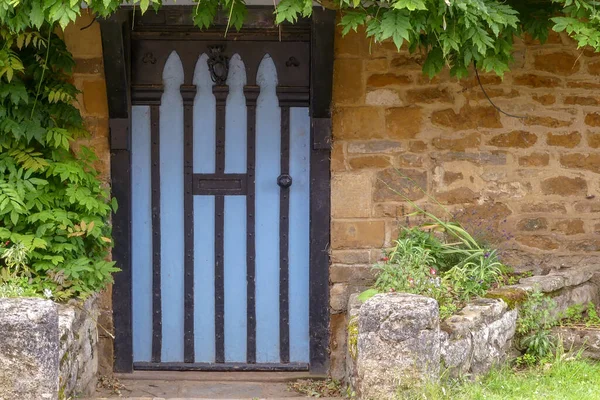 Old gothic painted portal set in a local stone wall under a wisteria. Stone entrance pillars. Old iron door furniture. Exterior landscape image with space for copy. Oxfordshire, England.