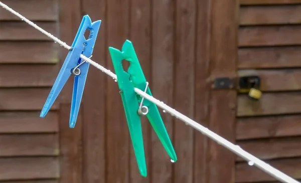 Mavi plastik mandal yağmur yağdıktan sonra çamaşır ipine baş aşağı asılı duruyor. Benzer yeşil olan ön planda kasten odak dışı. Kırsal ahşap döşemeli su damlacıkları. İngiltere