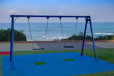 Çocuk parkında sallanan boş salıncak denizin arka planında.