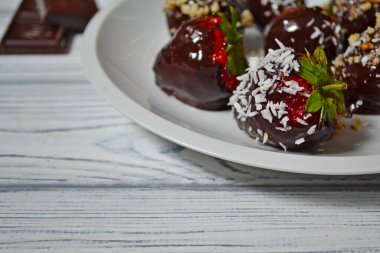 Mavi ahşap arka planda koyu çikolataya batırılmış taze çilekler.