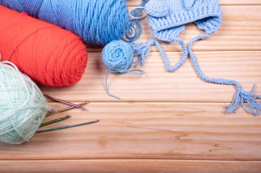 Ahşap arka planda kırmızı ve mavi örgü ipliği, iğneler ve yeni doğan şapkası.