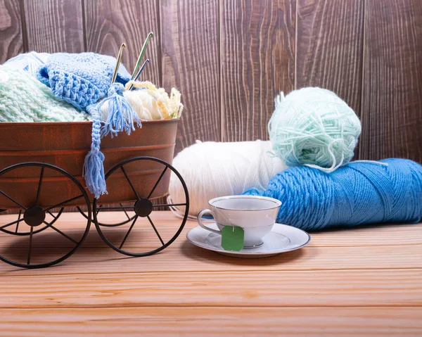 Knitting yarn and needles on Metal basket with coffee cup over wood Background.