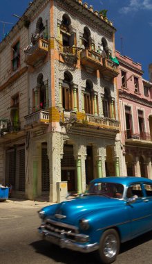 Küba 'nın La Havana şehrinin arka planında köhne renkli bir binası olan eski püskü mavi bir araba.
